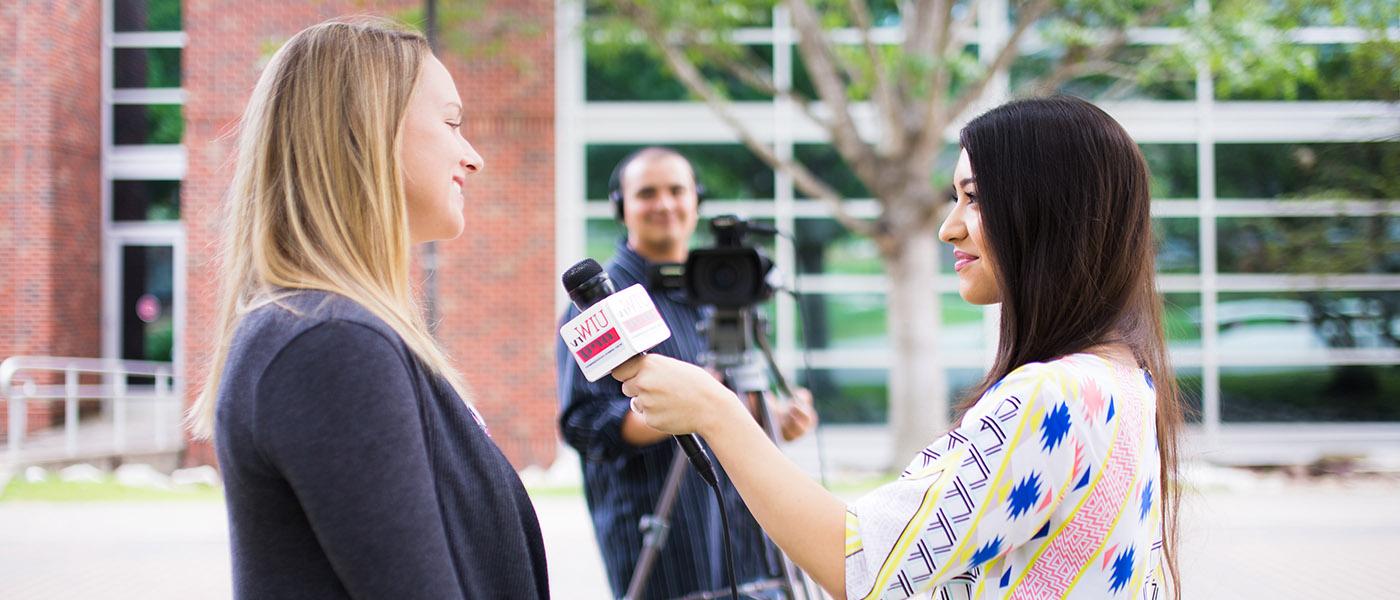 broadcasting student holding a microphone conducting an interview in front of a cameraman